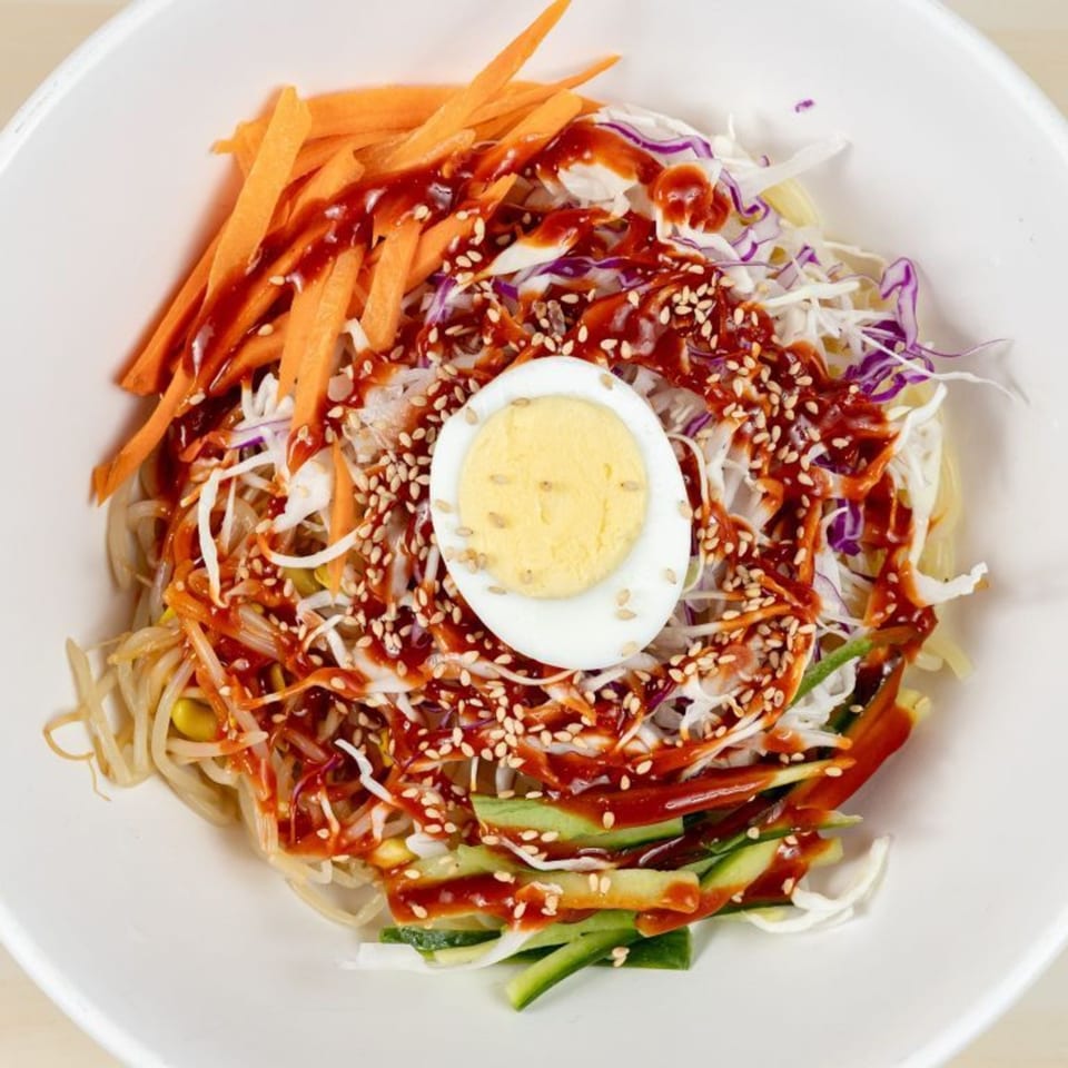 Mandurang's Korean bibim guksu with noodles, vegetables, gochujang sauce, sesame seeds, and a hard-boiled egg.